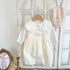 Baby girl's loose adjustable suspender romper in apricot and white, displayed on a wooden hanger with a beige hat and a mirror in the background.