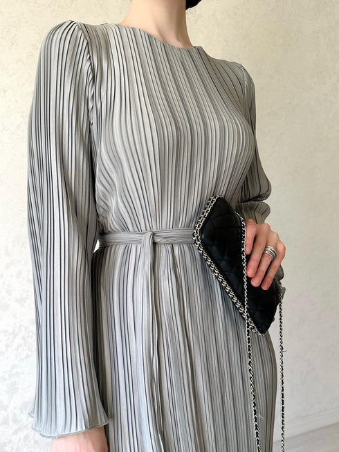 A woman wearing an elegant pleated bell sleeve mid-length grey dress with a mid-waist.