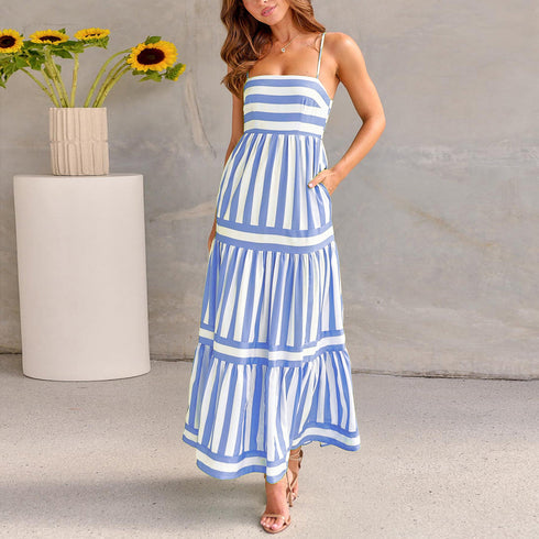 A woman standing in a sunny location wearing a white and blue striped long dress with no sleeves and a square neckline.