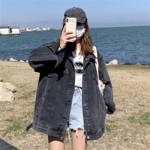 A lady posing for a picture holding her phone wearing a loose denim jacket with a cap, mask, and sunglasses.
