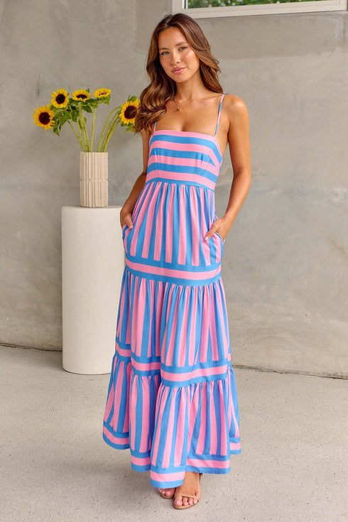 A woman standing in a sunny location wearing a pink and blue striped long dress with no sleeves and a square neckline.