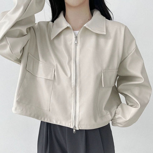 A woman wearing a long sleeve short coat in white, with a relaxed fit, cropped jacket style, and a zipper down the center. She is also wearing a white top and beige skirt.